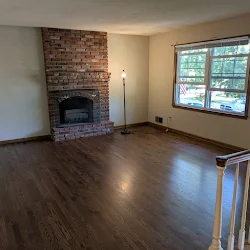 Empty living room with fireplace, hardwood floors, and large windows