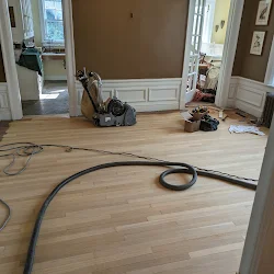 Construction site with coiled black electrical cord on hardwood floor and tools in background