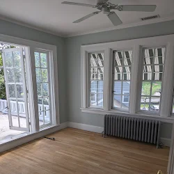 Empty room with hardwood floor, ceiling fan, glass doors, windows, and radiator heater