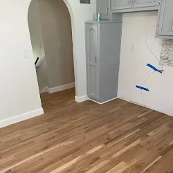 Empty room with wood flooring, white walls, and gray HVAC unit in corner
