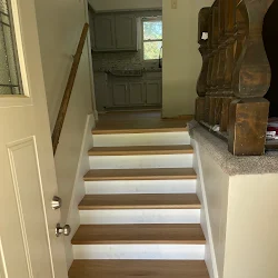 Wooden and white painted staircase descending to basement door with wooden furniture visible