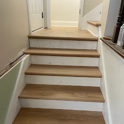 Wooden staircase with white walls leading to an open doorway at the top