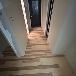 Hallway with wood-look plank flooring and white walls leading to dark door