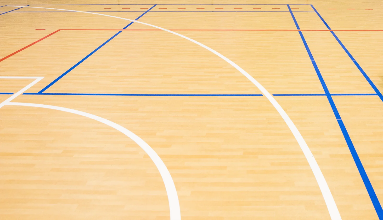 Wooden gymnasium floor with blue boundary lines, white curved markings, and red line visible in corner