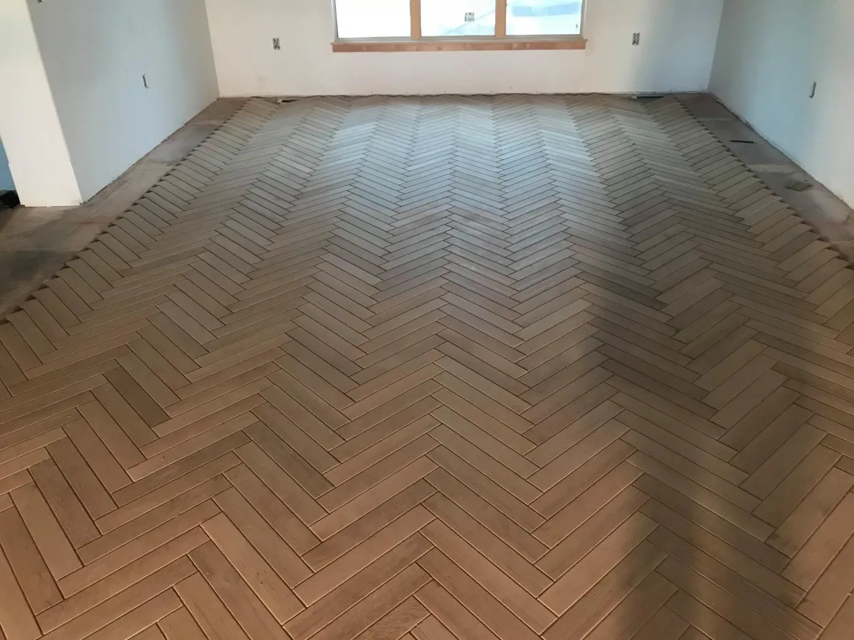 Herringbone wood flooring installed in empty room with white walls and windows
