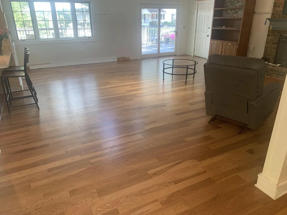 Spacious living room with hardwood floors, large windows, glass door, and minimal furniture