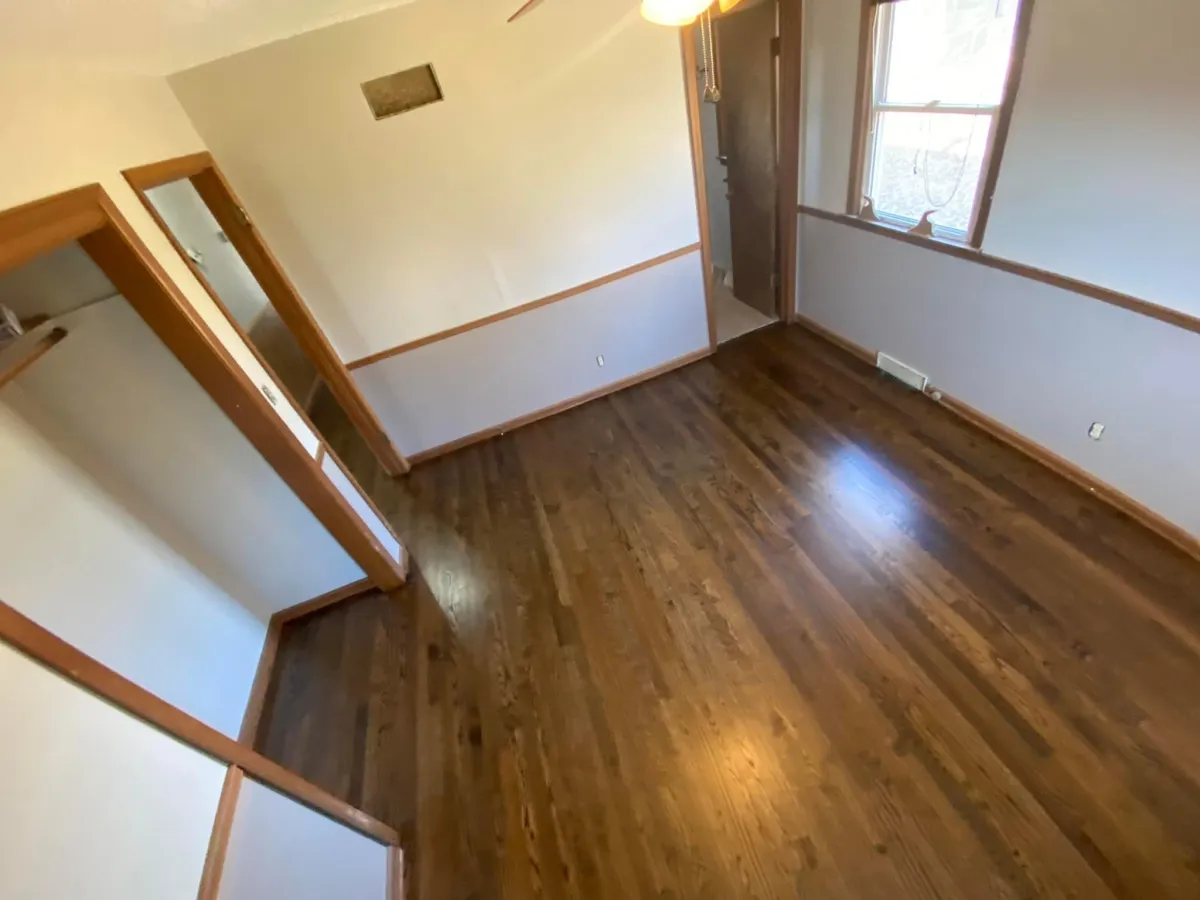 Empty bedroom with hardwood floors, wooden trim, and two-tone walls with window